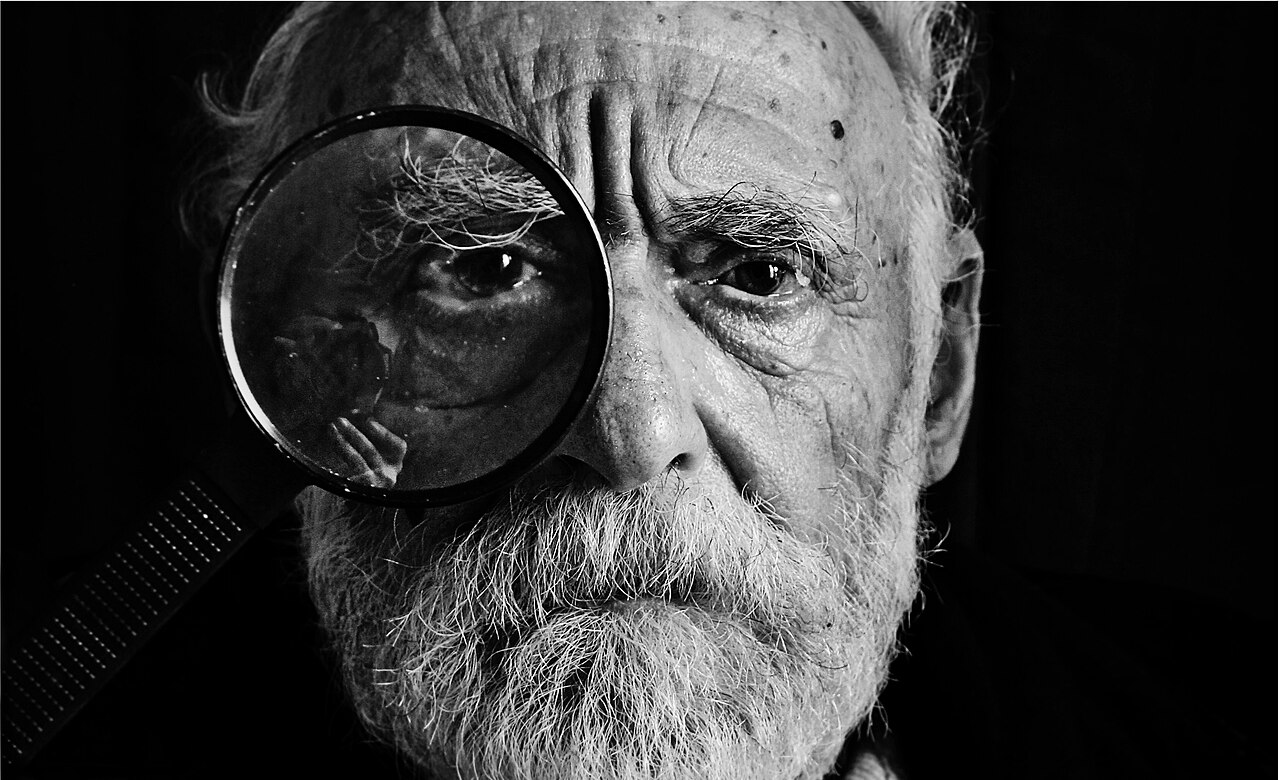 An older man looking closely at something through a magnifying glass