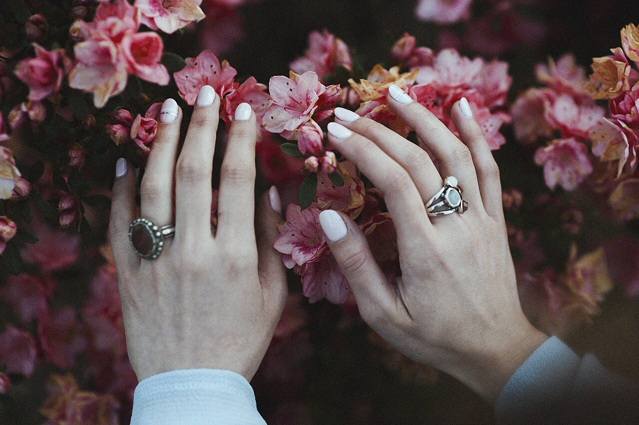 Two hands wearing stone-set rings against pink blossoms